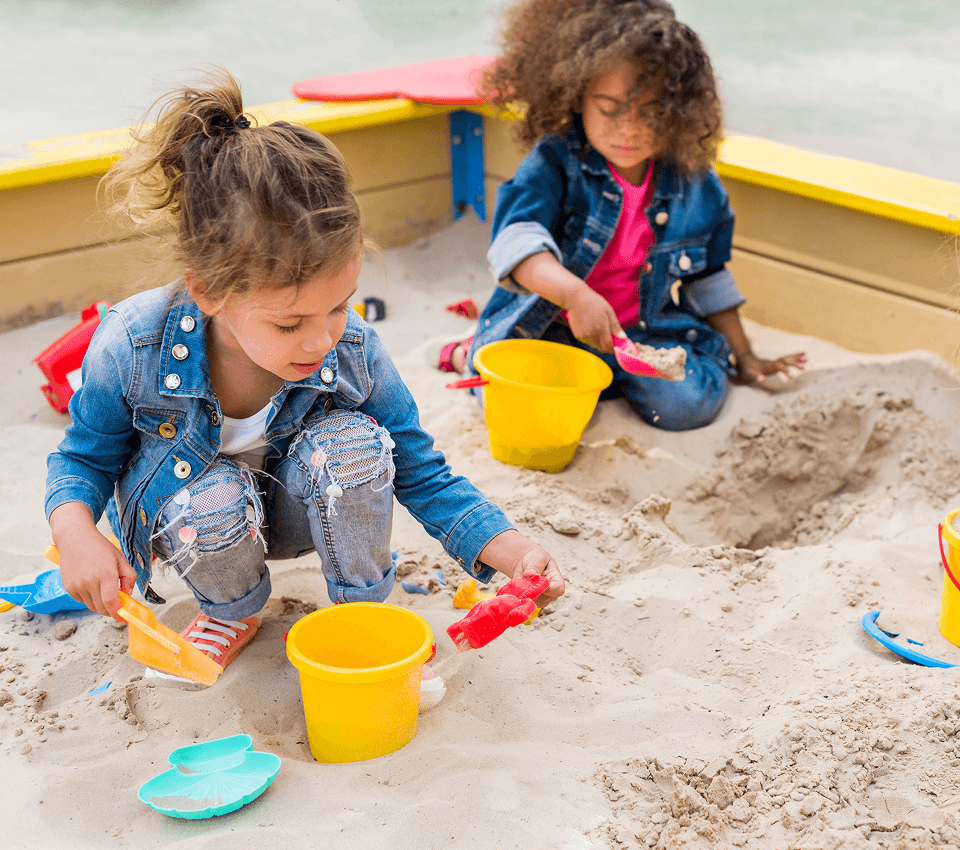 Two preschool girls playing together in a sandbox at a playground.