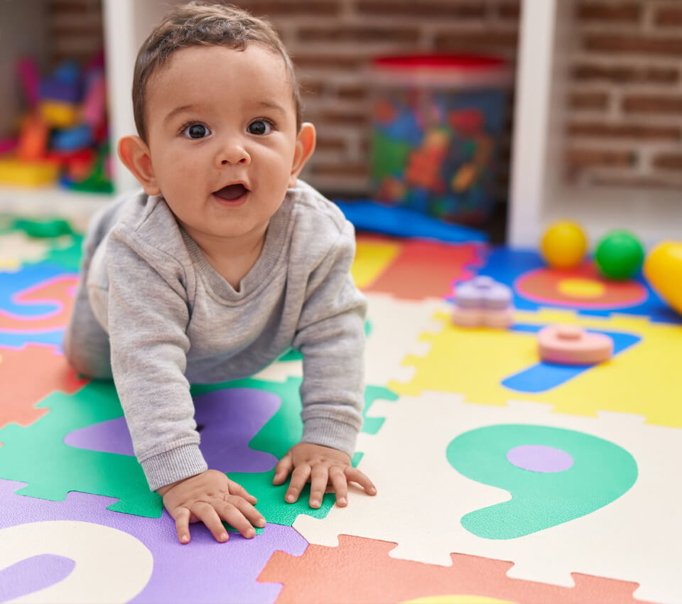 Infant crawling on a colorful numbered mat at a daycare.