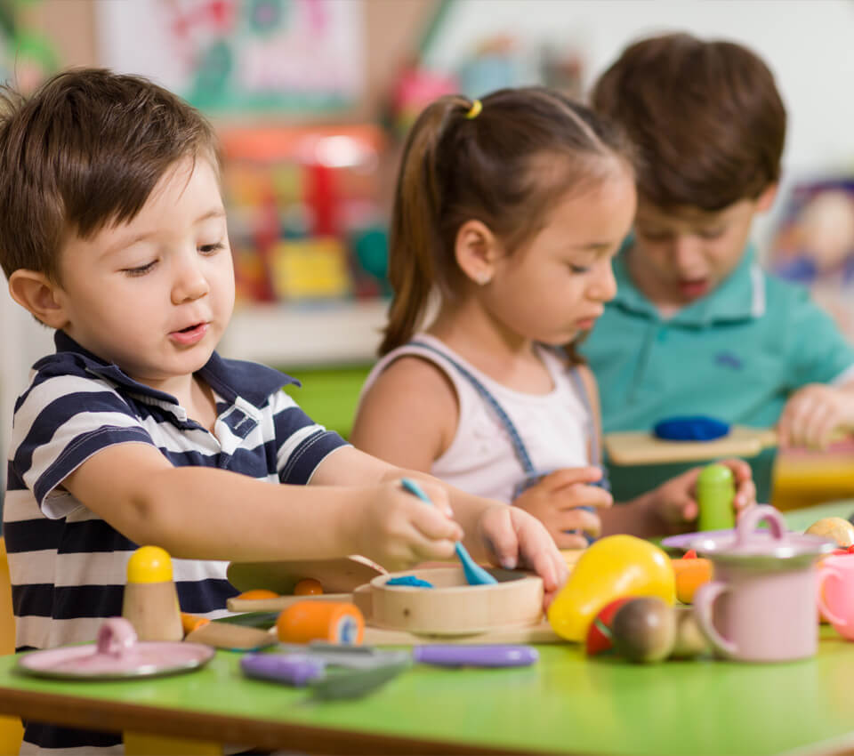 Preschool children playing and learning together at a classroom table.