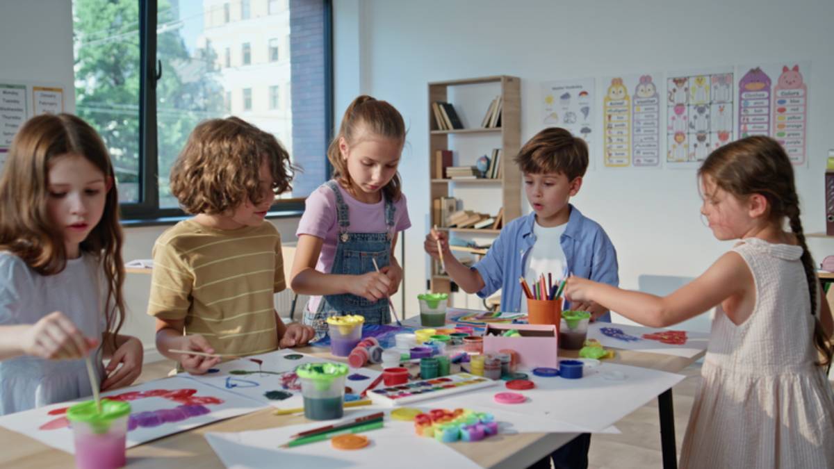 Pupils creating colorful art at collaborative workshop with vibrant materials. Boys girls working on painting projects at lesson classroom. Children concentrating on teamwork enjoying creativity.